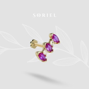 Könnte beinhalten: Goldfarbener Ohrring mit drei magentafarbenen, marquiseförmigen Edelsteinen und zwei kleineren, runden, klaren Edelsteinen. Der Ohrring hat einen Steckerverschluss. Das Wort "SORIEL" ist hellgrau gedruckt.