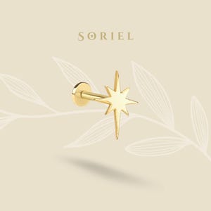 Puede incluir: Un pendiente dorado en forma de estrella con una parte trasera plana y un poste. El pendiente tiene un diseño de estrella con ocho puntas. El nombre de la marca "SORIEL" se muestra en la parte superior de la imagen.