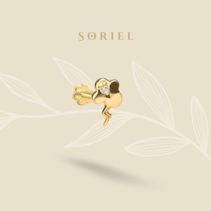 May include: A gold-colored earring with a lightning bolt design and a small, clear gemstone. The earring has a post back and a decorative flower-shaped front. The brand name "SORIEL" is displayed in gold lettering.