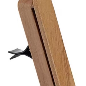 Peut inclure: Un diffuseur d'air pour voiture en bois avec une pince noire. Le diffuseur est rectangulaire avec des bords arrondis et possède une fente pour insérer une recharge parfumée.
