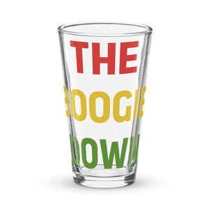 Könnte beinhalten: Ein klares Bierglas mit den Worten "THE BOOGIE DOWN" in roten, gelben und grünen Blockbuchstaben. Das Glas ist leer und steht auf einer weißen Oberfläche.