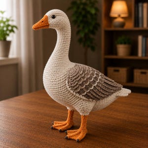 May include: A crochet goose plush toy featuring a cream-colored body, a bright orange beak and webbed feet, and textured brown wing feathers. The stuffed animal has a long neck, a rounded head, and a single black bead eye visible on the side.