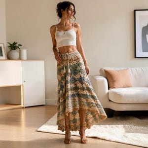 Puede incluir: Un top corto blanco sin mangas con tirantes finos y una falda larga de ganchillo con corte asimétrico, que presenta un patrón geométrico multicolor en tonos beige, azul y crema, con cintura de cordón y un detalle de dobladillo festoneado.