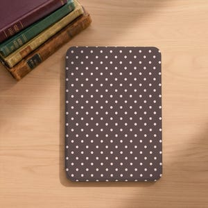 May include: A rectangular, dark brown case with a white polka dot pattern. The case is on a light brown wooden surface, with a stack of antique books in the upper left corner.
