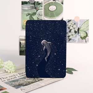 May include: A navy blue rectangular card featuring a white whale shark illustration against a starry night sky. The design includes a dark blue path and white stars. The card is surrounded by decorative elements.
