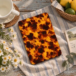 May include: A rectangular tablet case featuring a glossy, marbled tortoiseshell pattern in shades of deep brown and vibrant amber. The surface is smooth and reflective, showcasing a swirling, organic design across the entire front panel.