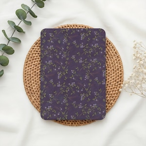 May include: A rectangular tablet cover featuring a deep purple background with a repeating pattern of small, delicate light purple flowers and thin green stems with leaves. The cover has rounded corners and a smooth, matte-like surface texture.