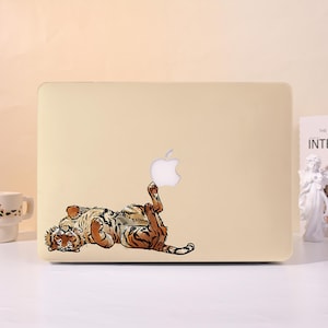 May include: A light beige laptop cover featuring a graphic illustration of a tiger lying on its back. The tiger is depicted with orange and black stripes, white fur on its belly, and its paws raised towards the centre Apple logo on the laptop.