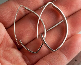 Puede incluir: Un par de pendientes de aro de plata en forma de lágrima. Los pendientes están hechos de un metal delgado y plano y tienen un acabado liso y pulido.