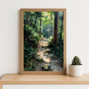 Op de afbeelding: Een ingelijste prent van een bospad. Het kunstwerk toont een zonovergoten pad dat door een weelderig groen bos slingert. Het pad is gemaakt van stenen en de bomen zijn hoog en slank. Het kunstwerk zit in een houten lijst.