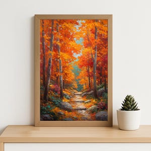 May include: A framed landscape painting of an autumnal forest path. The artwork showcases vivid orange and red leaves, with a path meandering through the trees. The painting is set in a light brown wooden frame, and is displayed on a light brown wooden surface.