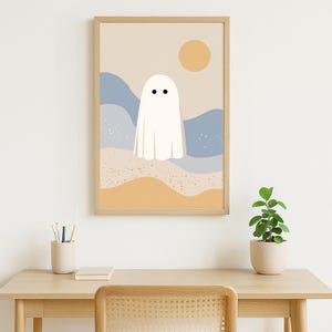 May include: A framed art print with a minimalist illustration of a white ghost with two black dots for eyes. The background features beige, blue, and yellow abstract shapes, with a yellow sun in the upper right corner.