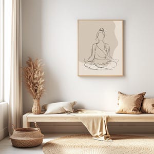 May include: A framed line art print depicting a person in a seated yoga pose. The artwork has a minimalist style with a beige background and a light wood frame. The room includes a wooden bench, cushions, and a woven basket.