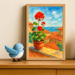 May include: Watercolor painting in a wooden frame depicts a red geranium in a terracotta pot on a balcony overlooking a coastal town. The sky is blue with white clouds. A blue bird figurine sits on a wooden surface.