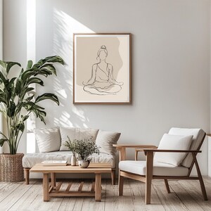 May include: A framed art print with a minimalist line drawing of a person in a seated meditation pose. The artwork is in a wooden frame and has a neutral colour palette with beige and brown tones. The print is displayed in a living room setting.