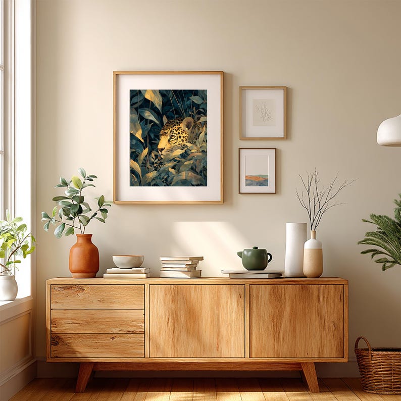 May include: A framed art print featuring a jaguar hidden in lush green foliage. The artwork has a natural wood frame and is displayed above a wooden cabinet with decorative items. The room has a neutral color palette.