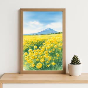 Op de afbeelding: Een ingelijste kunstdruk met een landschap. Een veld met gele bloemen vult de voorgrond, leidend naar een berg onder een blauwe lucht met wolken. Het kunstwerk zit in een lichtbruine houten lijst.