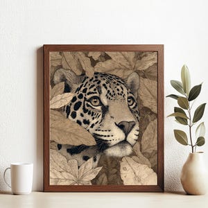 Könnte beinhalten: Ein gerahmter Sepia-Druck eines Jaguar-Gesichts, teilweise verdeckt von stilisierten Blättern. Der Jaguar hat schwarze Flecken und ist vor einem neutralen Hintergrund platziert. Eine weiße Tasse und eine Vase mit Grünzeug befinden sich im Vordergrund.