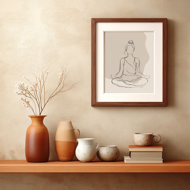 May include: A framed print with a minimalist line drawing of a person in a seated yoga pose. The artwork is in a brown wooden frame with a white mount. The image is displayed on a wooden shelf with vases, a cup, and books.