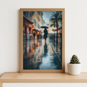 Könnte beinhalten: Ein gerahmter Druck einer regnerischen Straßenszene. Eine Person mit einem Regenschirm geht eine nasse Straße entlang, mit Reflexionen von Gebäuden und Lichtern. Der Rahmen ist hellbraun, und eine kleine Topfpflanze steht auf dem Regal.