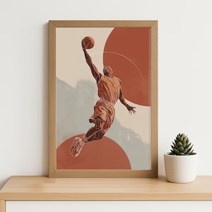 May include: A framed print depicting a basketball player in mid-air, about to dunk the ball. The artwork uses a line-art style with orange and brown tones. Two large orange circles are in the background. The frame is made of light-coloured wood.