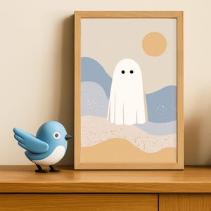 May include: A framed art print with a minimalist ghost illustration against a beige backdrop, blue waves, and a yellow sun. A blue bird ornament is placed on a wooden surface in front of the artwork.