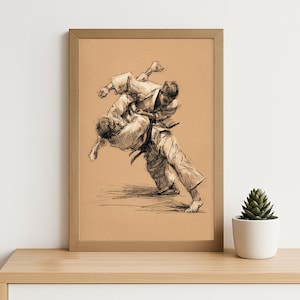 Op de afbeelding: Een ingelijste potloodschets van een Judo-wedstrijd. Twee figuren in Judo-uniformen zijn in een dynamische worp, tegen een bruine achtergrond. Het kunstwerk staat op een houten plank.