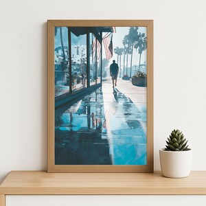 Peut inclure: Une impression d'art encadrée représentant une scène de rue ensoleillée avec une personne marchant sur un trottoir mouillé. Des palmiers et des drapeaux américains sont visibles. L'œuvre a un style aquarelle avec des tons bleus et bruns.