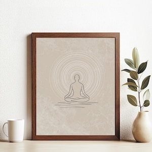 May include: A framed print featuring a minimalist line drawing of a person in a seated yoga pose. The artwork is set against a beige background with concentric circles, framed in a dark brown wooden frame. A white mug and a vase with greenery are in the foreground.