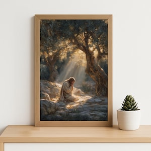 Puede incluir: Una impresión enmarcada representa a una persona arrodillada en oración bajo olivos, bañada por la luz del sol. La obra de arte presenta una paleta de colores cálidos y texturas detalladas, creando una escena serena y espiritual. La impresión se exhibe en una estantería de madera.