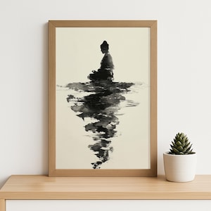 May include: A framed art print featuring a black and white ink wash illustration of a person meditating. The artwork depicts a figure in a seated position, reflected in the water below. The frame is a light brown color.