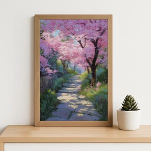 Peut inclure: Tableau encadré représentant un chemin pavé serpentant dans un jardin fleuri. Des arbres aux fleurs roses bordent le chemin. L'œuvre est dans un cadre en bois clair. Un petit cactus en pot est au premier plan.