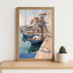 Puede incluir: Pintura a la acuarela de una escena portuaria con barcos atracados a lo largo de un muelle de piedra. La obra de arte presenta un marco de madera marrón claro, un mar azul, edificios blancos y un gato descansando en el muelle. Una pequeña planta suculenta en una maceta blanca está sobre una estantería de madera.