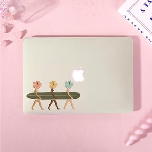 May include: A light-colored laptop case featuring a decal of three figures with hibiscus flower heads in shades of pink, yellow, and blue. Each figure is walking and carrying a long, dark green surfboard horizontally across their midsections.