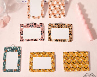 May include: Halloween-themed ID badge holders with various patterns, including ghosts, pumpkins, bats, and witch hats. The holders have a rectangular window for inserting an ID card and a metal loop at the top for attaching a lanyard.