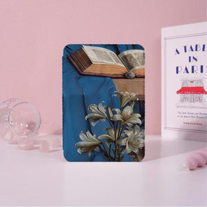 May include: A rectangular art print featuring a still life with a blue draped fabric, an open book, and white lilies. The print is set against a pink background with a book titled "A Table in Paris" visible.