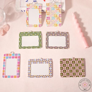 May include: A collection of floral-patterned ID badge holders in various colors, including pink, green, purple, and orange. Each holder has a clear window for displaying an ID and a decorative floral border. The holders are arranged on a pink surface.
