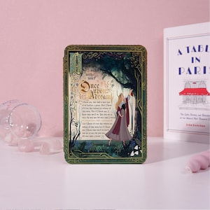 May include: A rectangular box with a fairytale theme. The box features the text "Once Upon a Dream" and an illustration of a couple dancing in a forest. The box has a green and gold border and is set against a pink background.