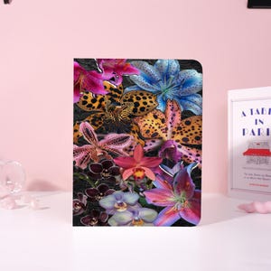 May include: A floral-themed notebook featuring a collage of vibrant orchid and lily blooms in shades of pink, purple, yellow, and blue against a dark background. The cover has a textured appearance, and the design is eye-catching.