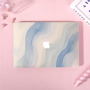 May include: A laptop hard shell case featuring a wavy, abstract pattern in shades of cream, beige, and muted blue. The design includes a central cutout that reveals the white Apple logo on the laptop lid, creating a smooth, layered aesthetic.