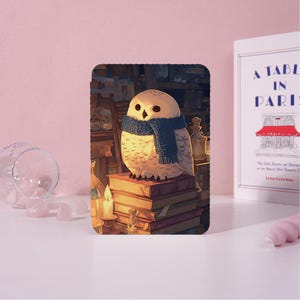 Op de afbeelding: Een rechthoekige tablethoes met een illustratie van een witte uil met een blauwe gebreide sjaal, zittend op een stapel boeken in een schemerige kamer met een brandende kaars, glazen flessen en planken op de achtergrond.