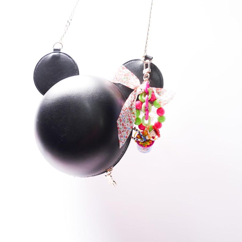 May include: A black leather purse shaped like Mickey Mouse's head with a pink and white floral ribbon and a colorful charm attached.