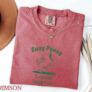May include: Crimson red t-shirt with a green cartoon lemon character and the text "Easy Peasy Lemon Squeezy".