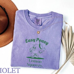 May include: A purple t-shirt with a green graphic of a cartoon lemon with the text "Easy Peasy Lemon Squeezy".