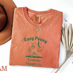 May include: A peach-colored t-shirt with a green graphic of a cartoon lemon with the text "Easy Peasy Lemon Squeezy."
