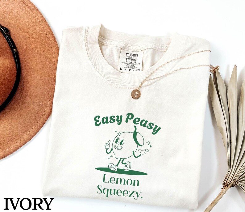 May include: Ivory t-shirt with a green graphic of a cartoon lemon with the text "Easy Peasy Lemon Squeezy."