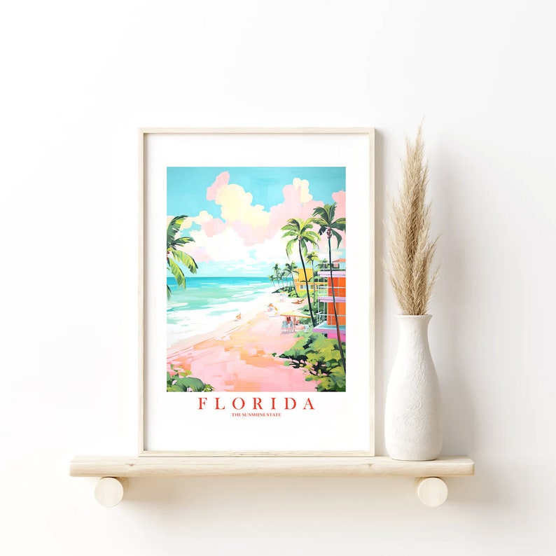 May include: A framed print of a colorful illustration of a beach scene in Florida. The print features palm trees, a pink sandy beach, turquoise water, and colorful buildings. The text "FLORIDA THE SUNSHINE STATE" is at the bottom of the print.