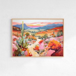 May include: A framed landscape painting of a desert scene. The artwork features a winding dirt road through a valley, with cacti, shrubs, and mountains in the background. The color palette includes pinks, oranges, greens, and blues, with a sunset sky.