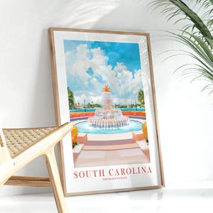 May include: A framed art print depicting a fountain with flowing water, set against a bright blue sky with white clouds. The text "SOUTH CAROLINA" is in red, with "THE PALMETTO STATE" underneath. The artwork is in a wooden frame.