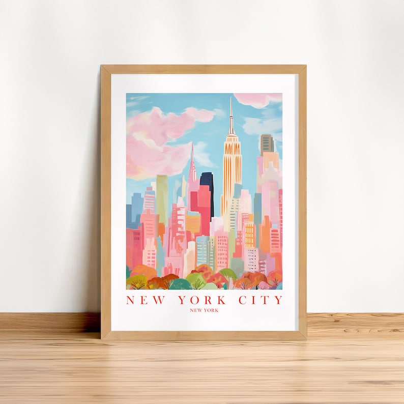 May include: A colorful illustration of the New York City skyline with the Empire State Building in the center. The illustration is framed in a light brown wood frame. The text "NEW YORK CITY" is printed below the image.